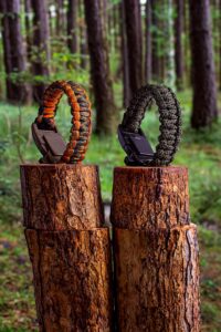 Bracelets de survie en paracorde exposés sur des bûches d'arbres dans un décor forestier.