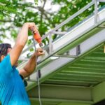 Un professionnel utilise une perceuse pour fixer des gouttières en aluminium blanches sur une structure de toiture métallique.