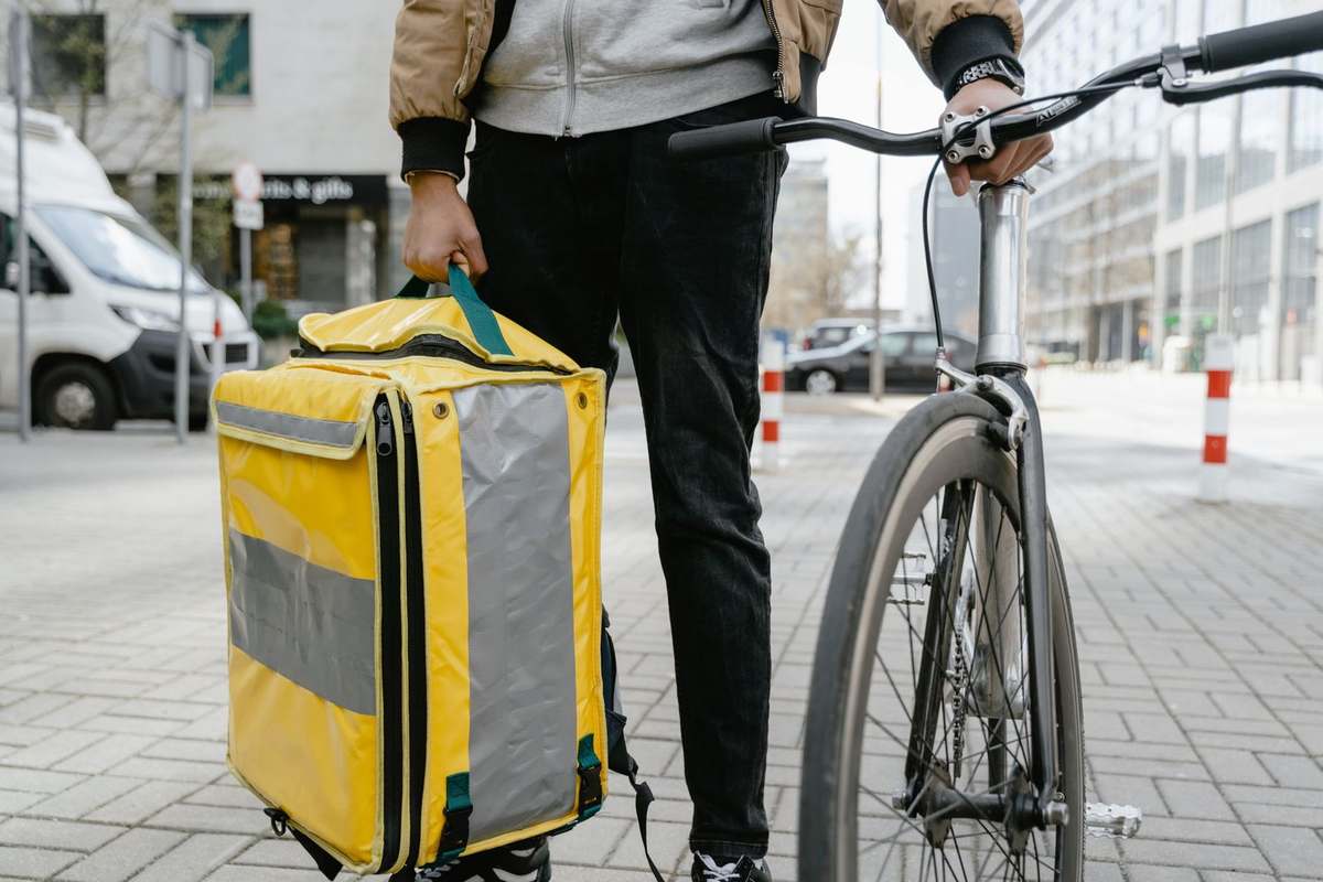 Personne avec sac jaune et vélo noir sur trottoir urbain