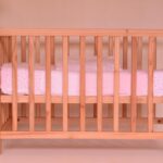 Un lit bébé en bois avec matelas rose dans une chambre