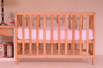 Un lit bébé en bois avec matelas rose dans une chambre