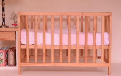 Un lit bébé en bois avec matelas rose dans une chambre